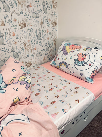 Children's bed with pink bedding and unicorn-themed pillow and a Quiet Kingdom Mattress Bed Sheet Protector