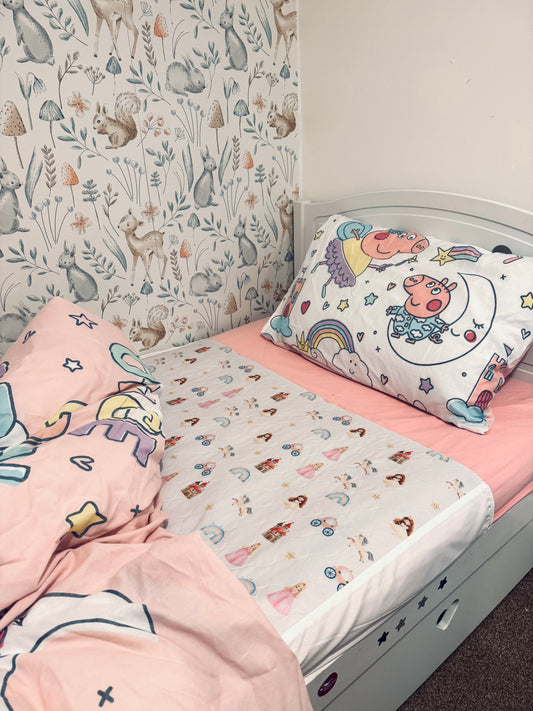 Children's bed with pink bedding and unicorn-themed pillow and a Quiet Kingdom Mattress Bed Sheet Protector
