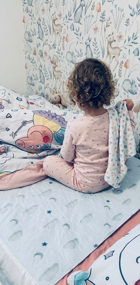 Child sitting on a bed with colourful bedding and pillows in a room with patterned wallpaper and Sleepy Stars     Mattress Bed Sheet Protector